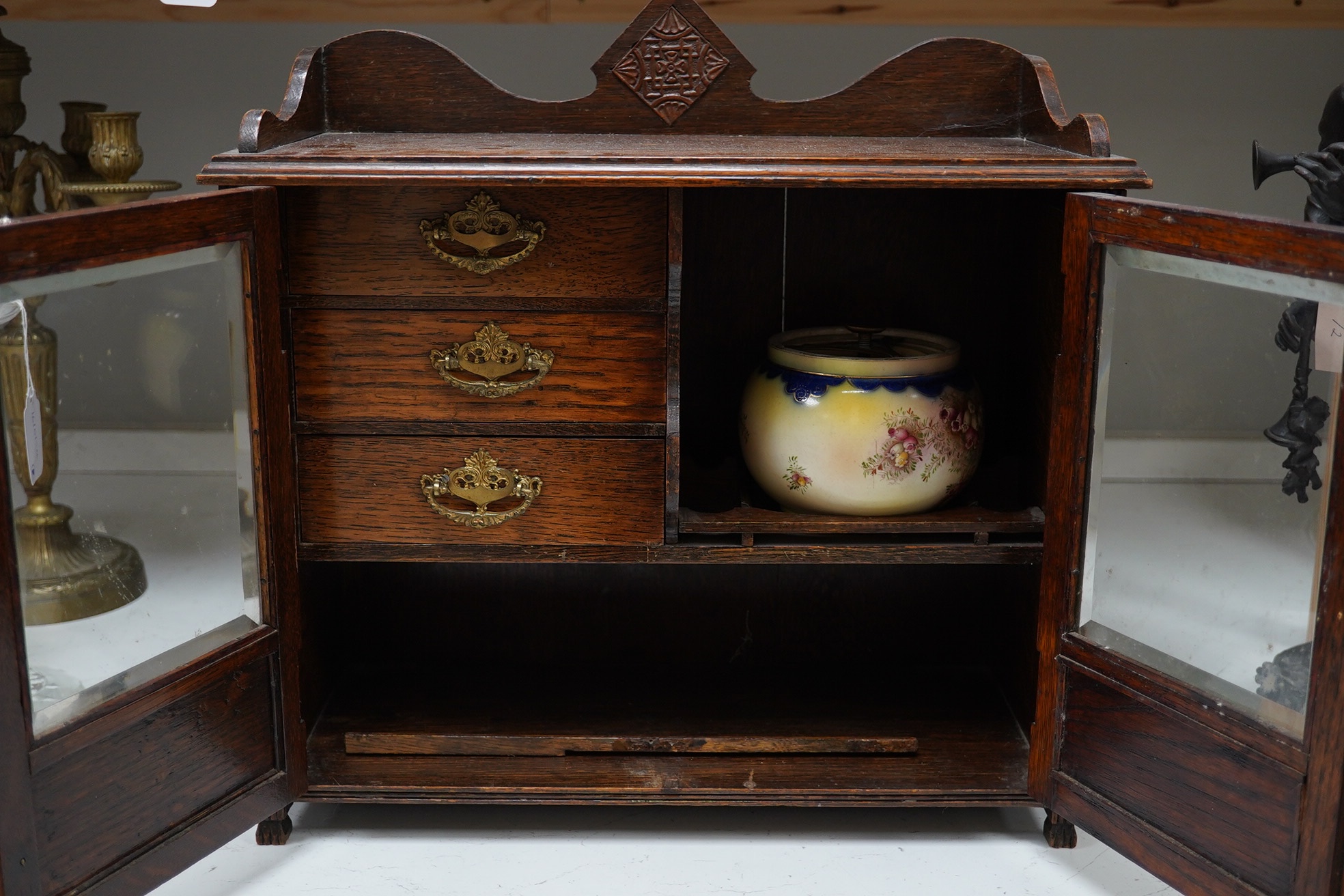 A carved oak smokers cabinet with Cartonware tobacco jar, cigar pricker and amber mouthpiece, 42cm wide. Condition - fair to good